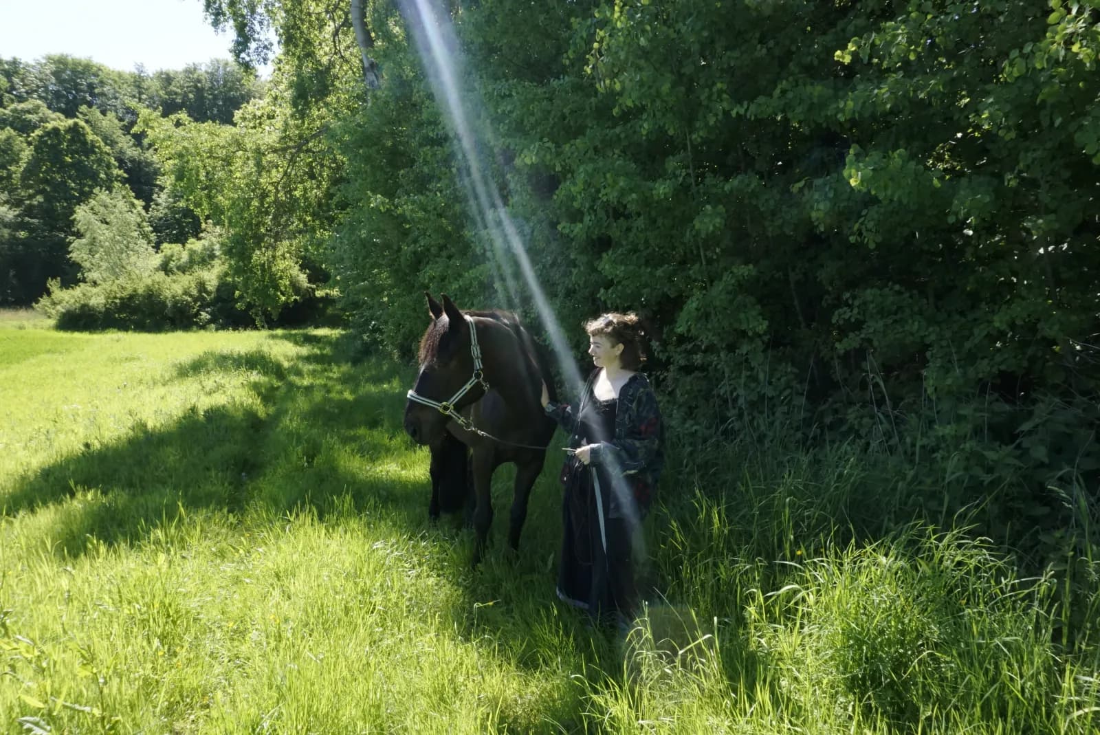 Fiete geht mit einem dunklen Pferd am Halfter über eine sommerliche Wiese am Waldrand