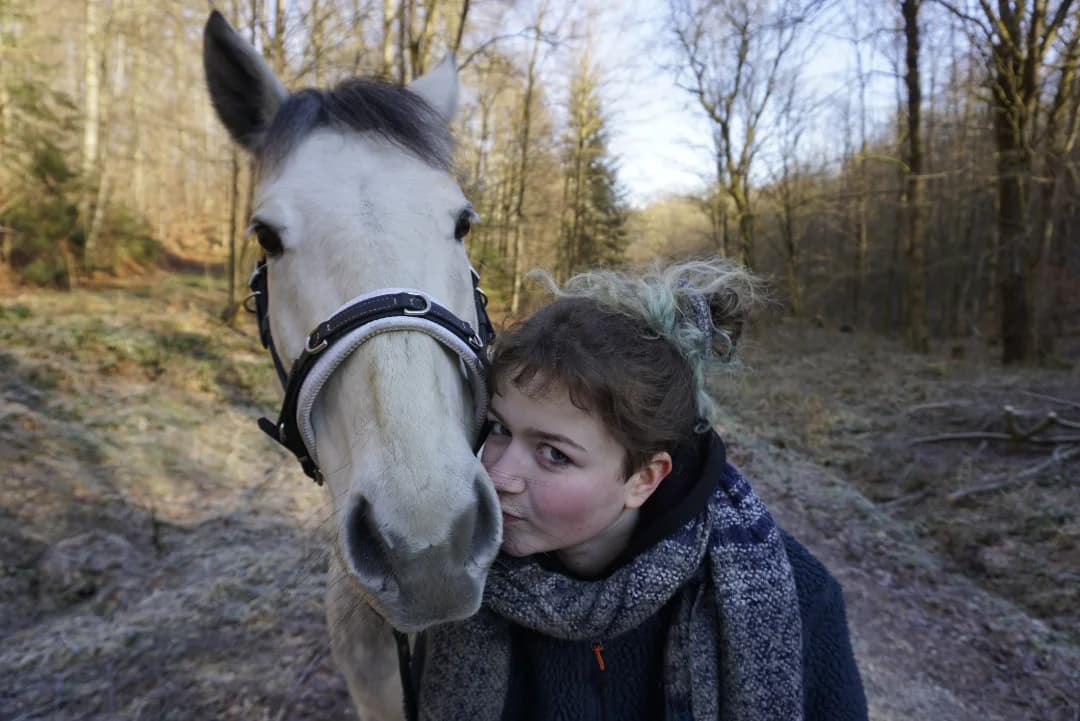 Trainerin und weißes Pferd zusammen, zeigt ihre enge Verbindung im Wald